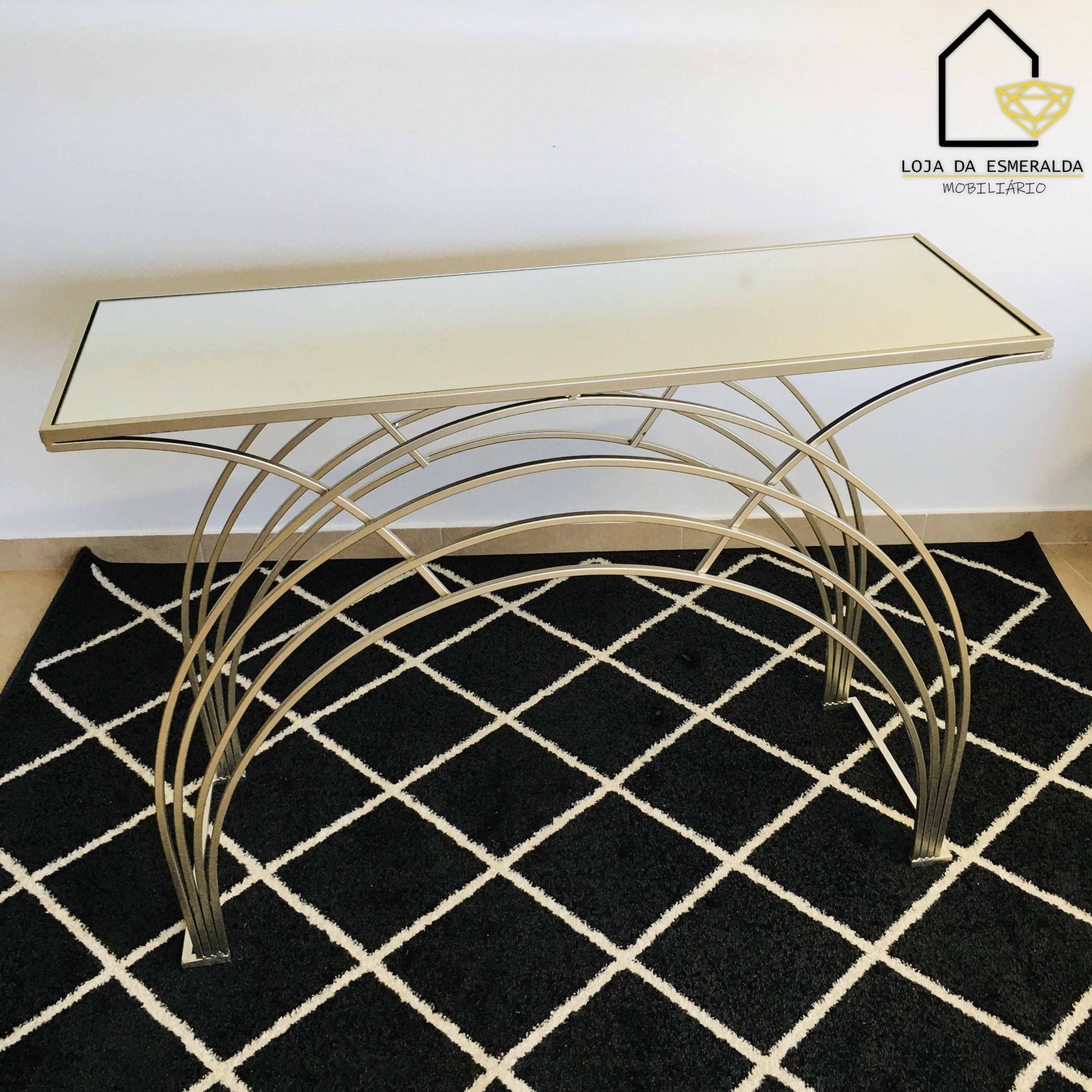 Mesa consola com tampo branco e estrutura metálica dourada sobre tapete preto com padrão branco
