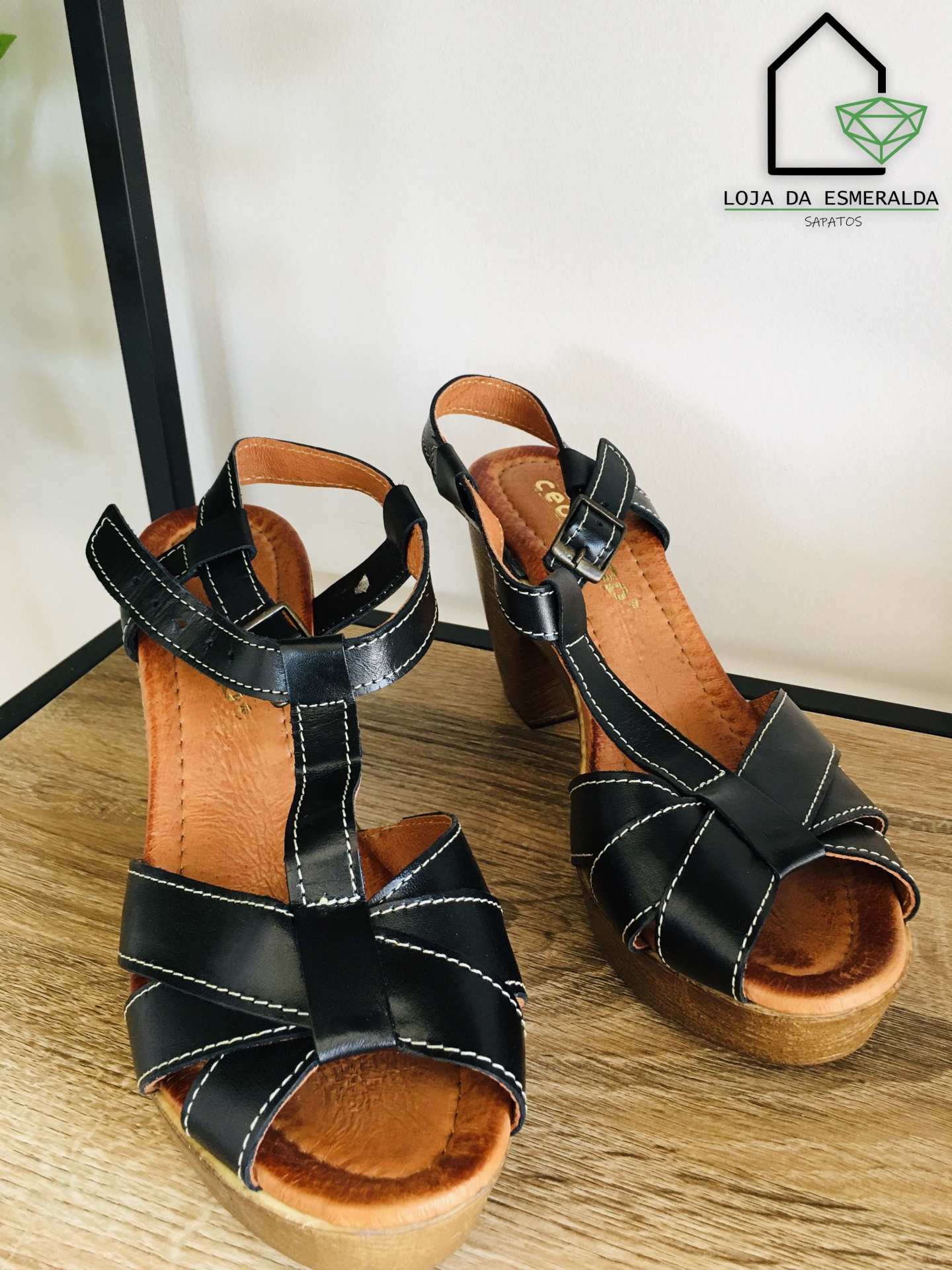 Sandálias pretas em pele com plataforma castanha, fecho de fivela, sobre madeira