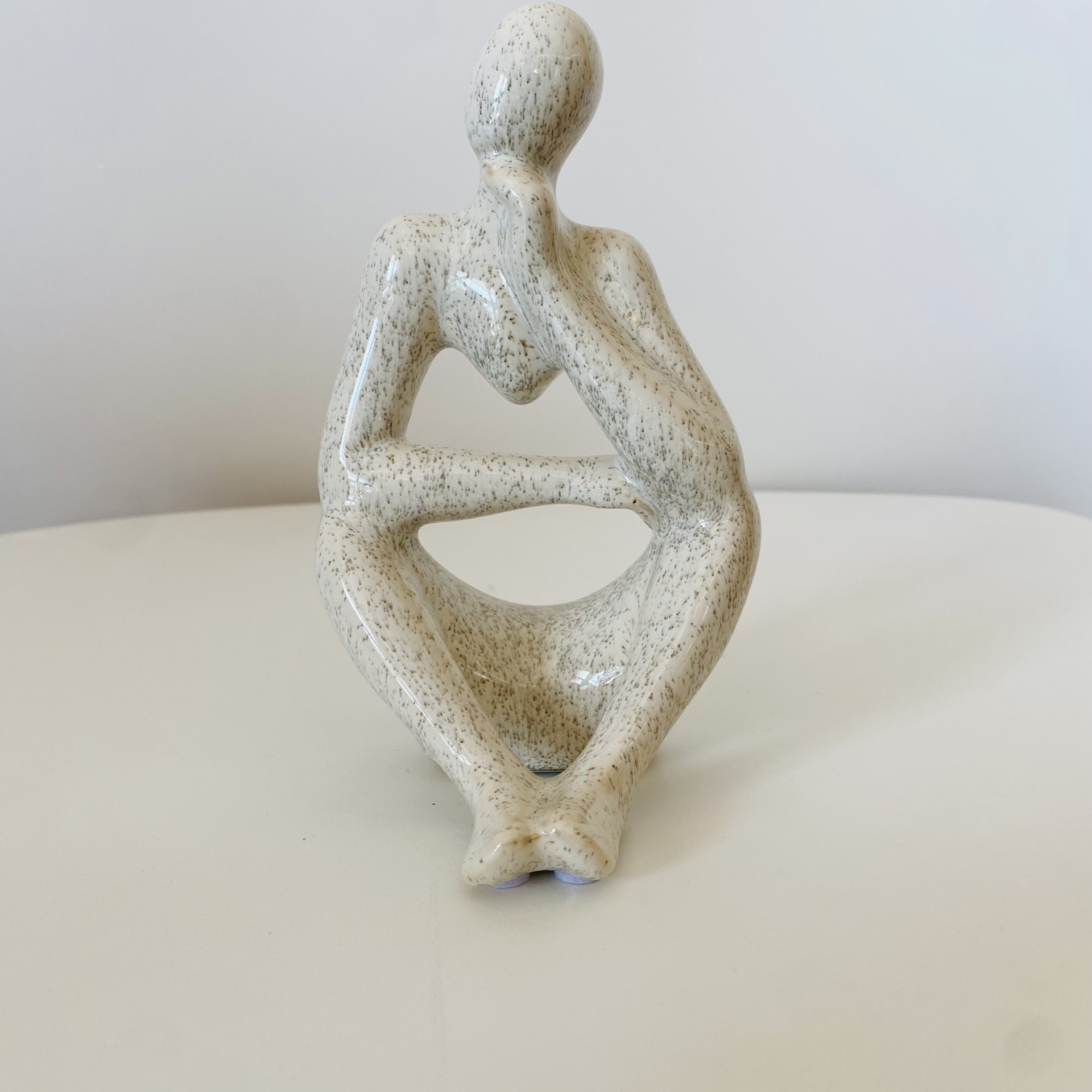 Escultura decorativa abstrata creme em forma de figura humana sentada com mão na cabeça