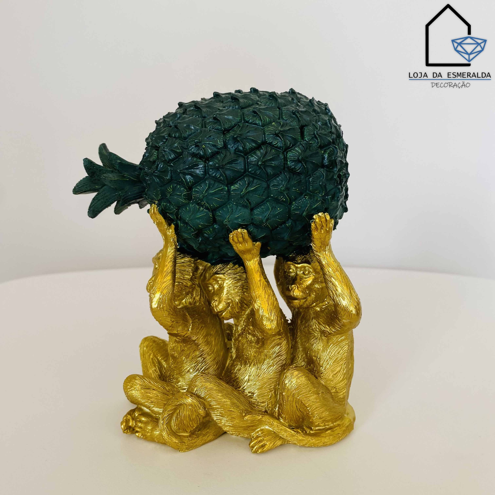 Escultura de três macacos dourados segurando um abacaxi verde escuro