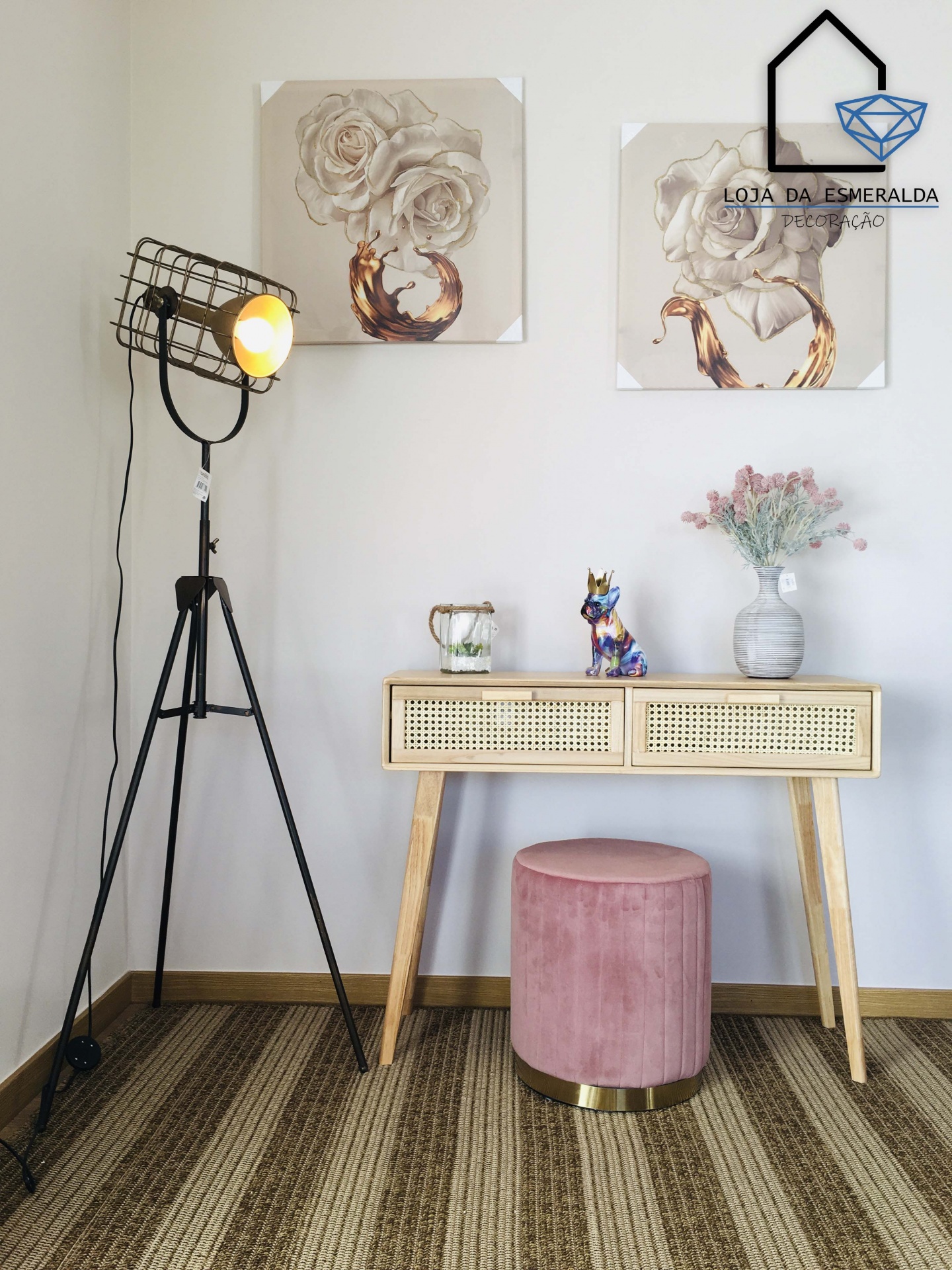 Candeeiro de pé industrial preto, mesa de consola em madeira clara com decoração floral, banquinho rosa estofado e obras de arte com flores