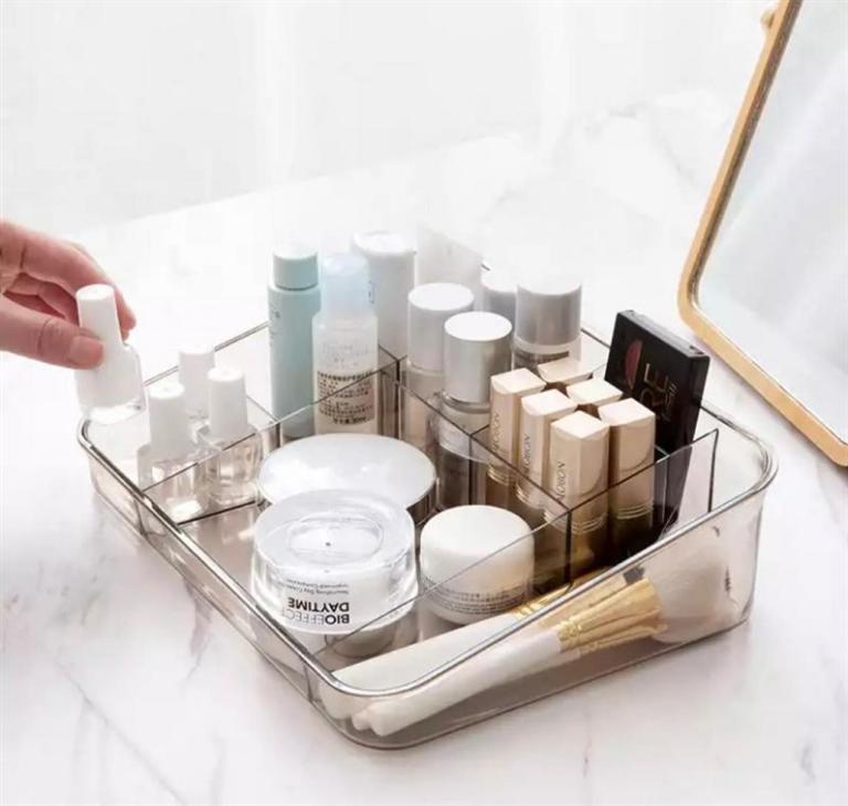 Organizador acrílico transparente com cosméticos e pincéis ao lado de espelho