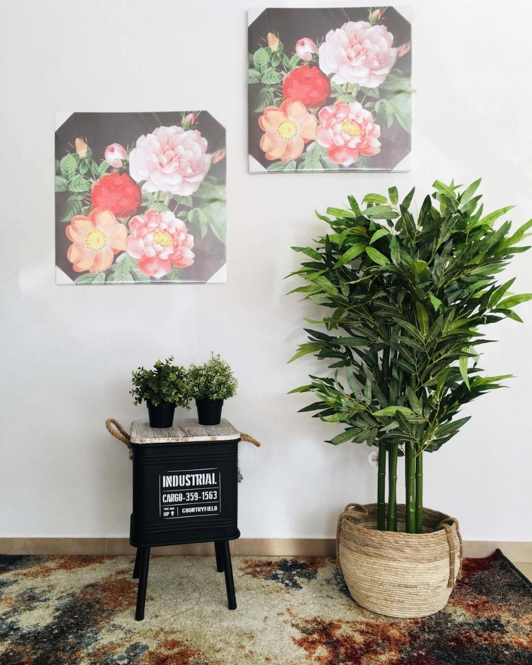 Decoração interior com telas de flores, mesa preta com texto INDUSTRIAL, plantas em vasos pequenos e planta alta num vaso de tecido.