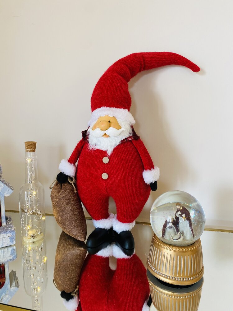 Figura decorativa de Pai Natal com roupa vermelha e saco castanho num ambiente com globo de neve e garrafa de vidro