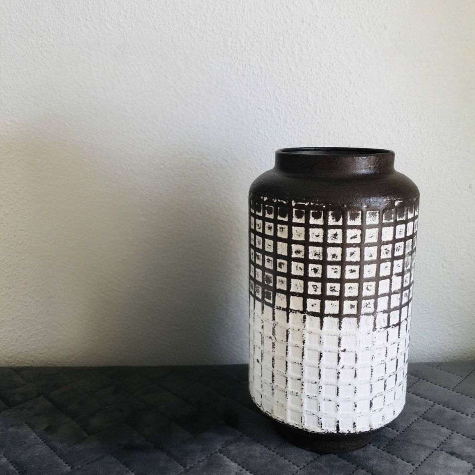Vaso cerâmico castanho com padrão branco quadriculado sobre superfície cinza escuro