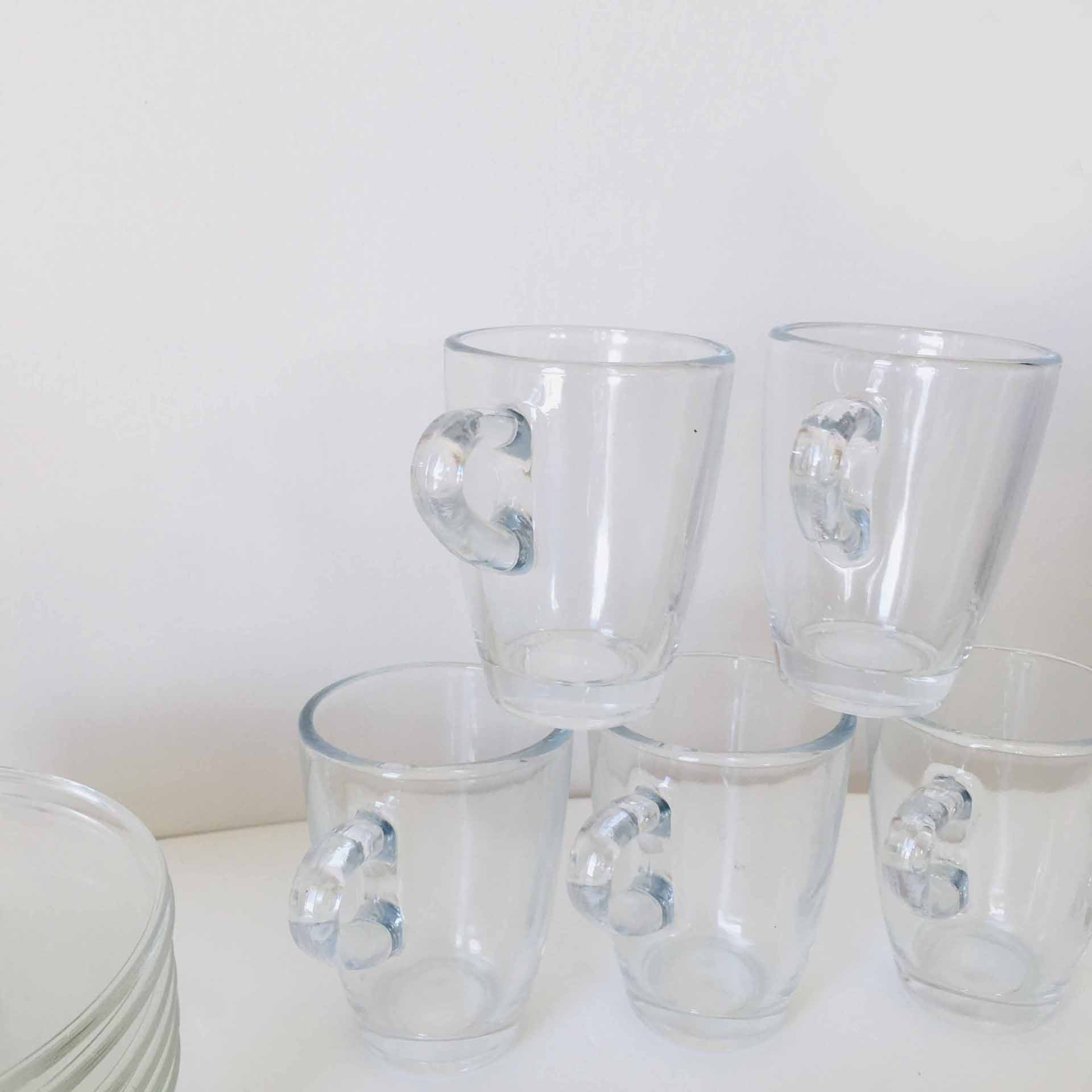 Seis copos de vidro transparentes com pega empilhados sobre superfície branca.