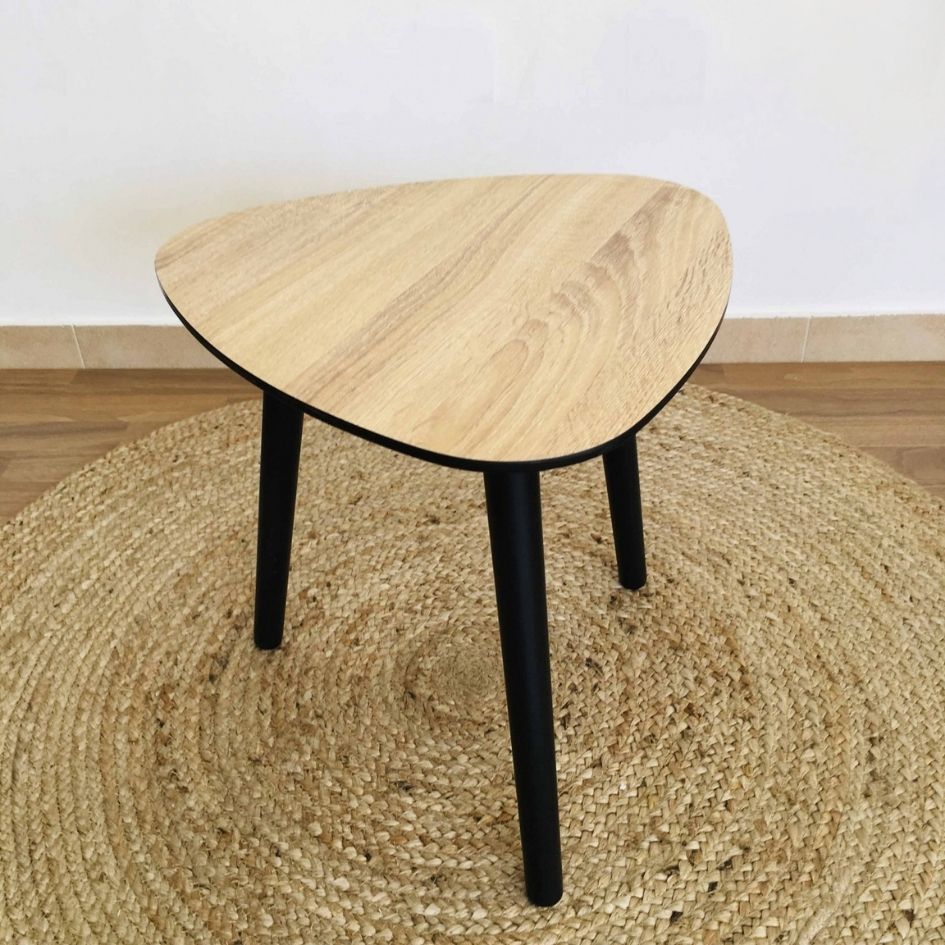 Mesa triangular de madeira clara com pernas pretas sobre tapete redondo de fibras naturais