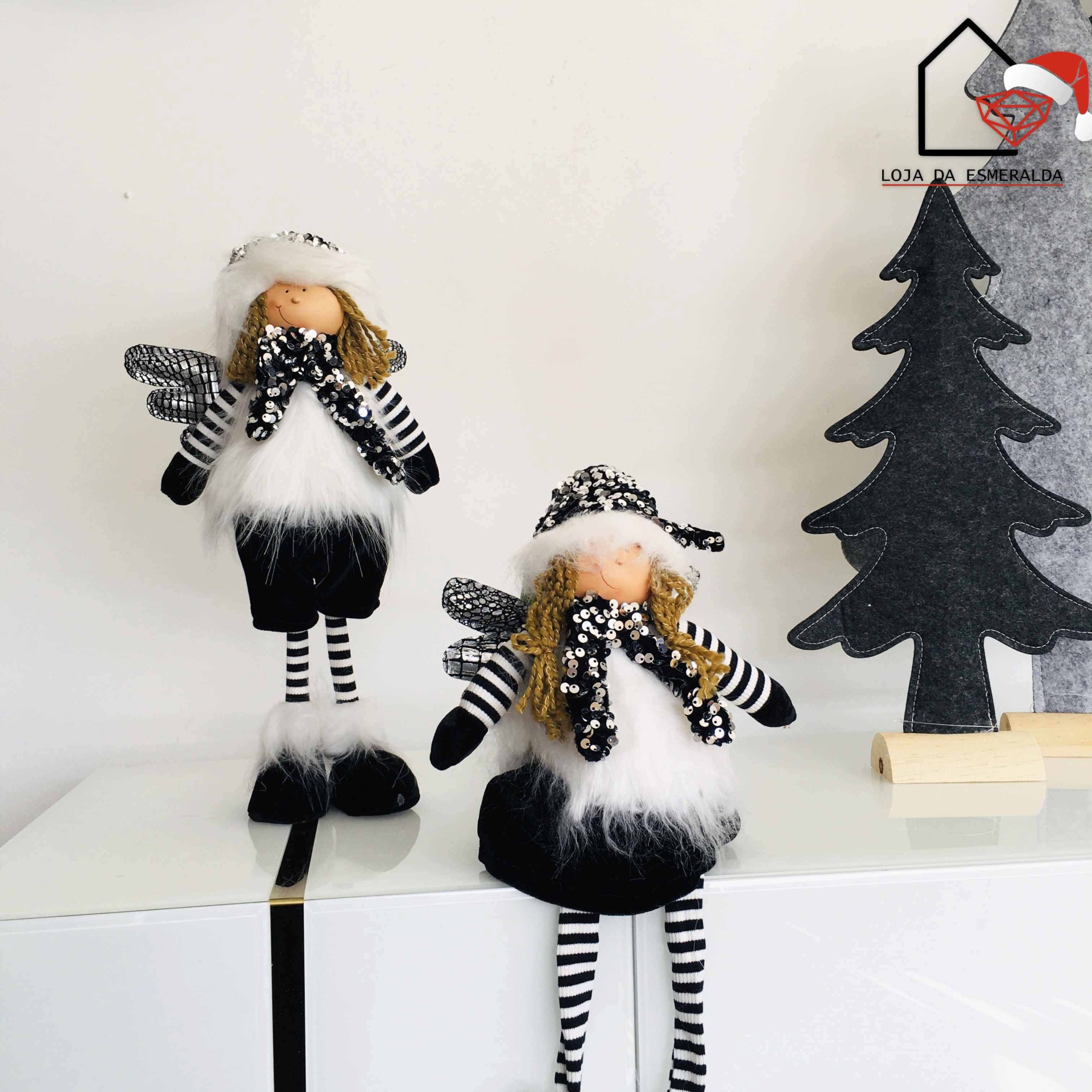 Duas figuras decorativas de anjos com roupas pretas e brancas ao lado de árvore decorativa preta