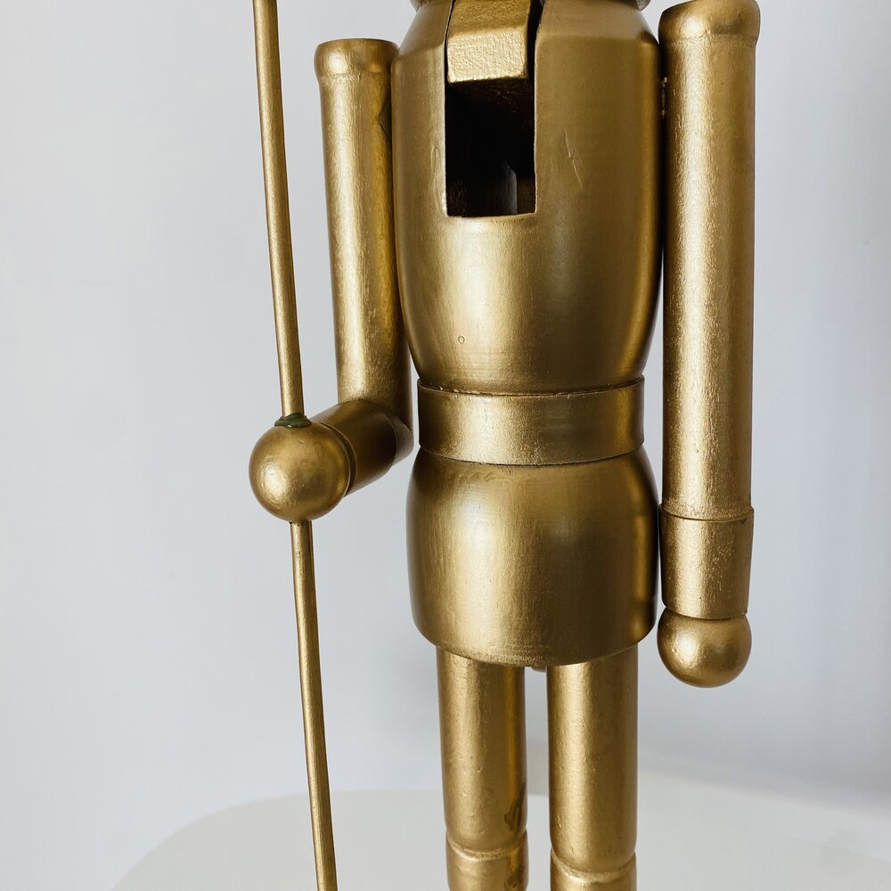 Boneco de madeira dourado segurando uma vara em fundo branco