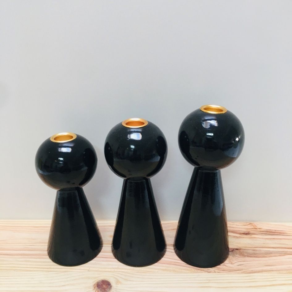 Três castiçais pretos brilhantes com interior dourado em diferentes tamanhos sobre superfície de madeira.