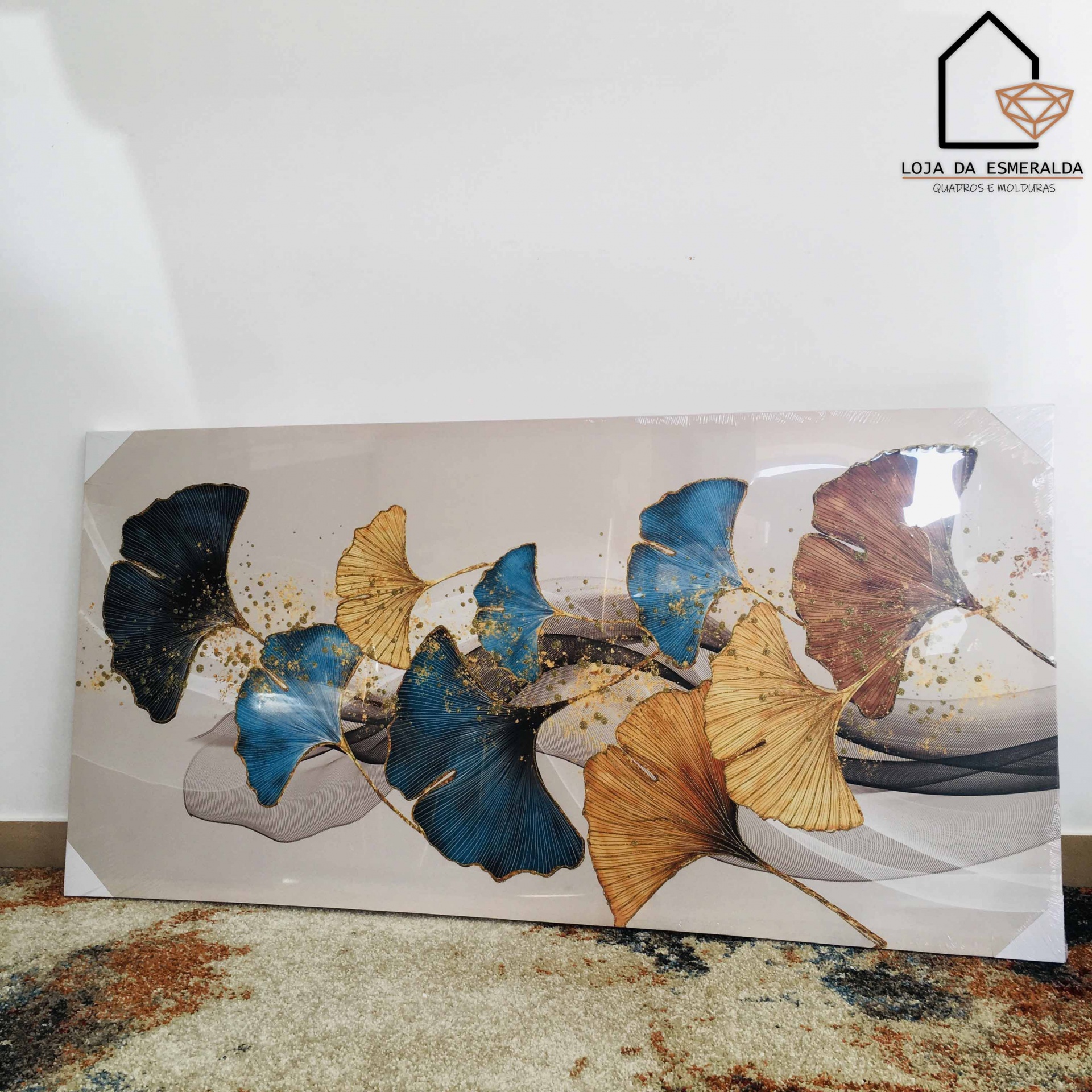 Quadro decorativo de folhas em cores azul, dourado, preto e castanho com logotipo Loja da Esmeralda