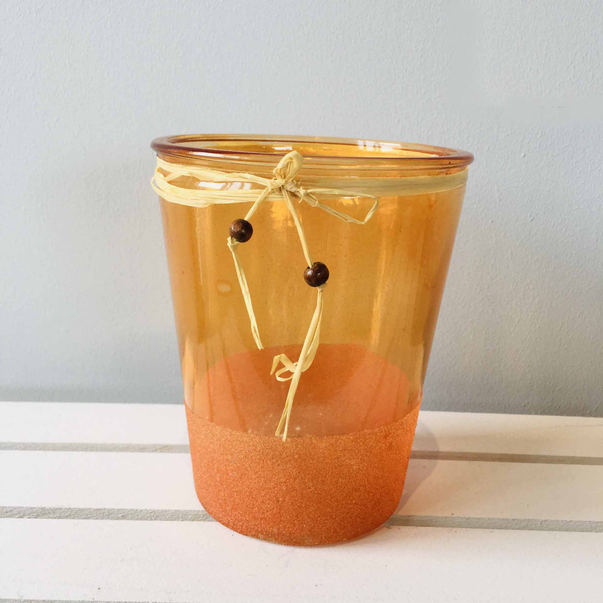 Vaso de vidro âmbar com base granulada e laço de ráfia com contas de madeira.