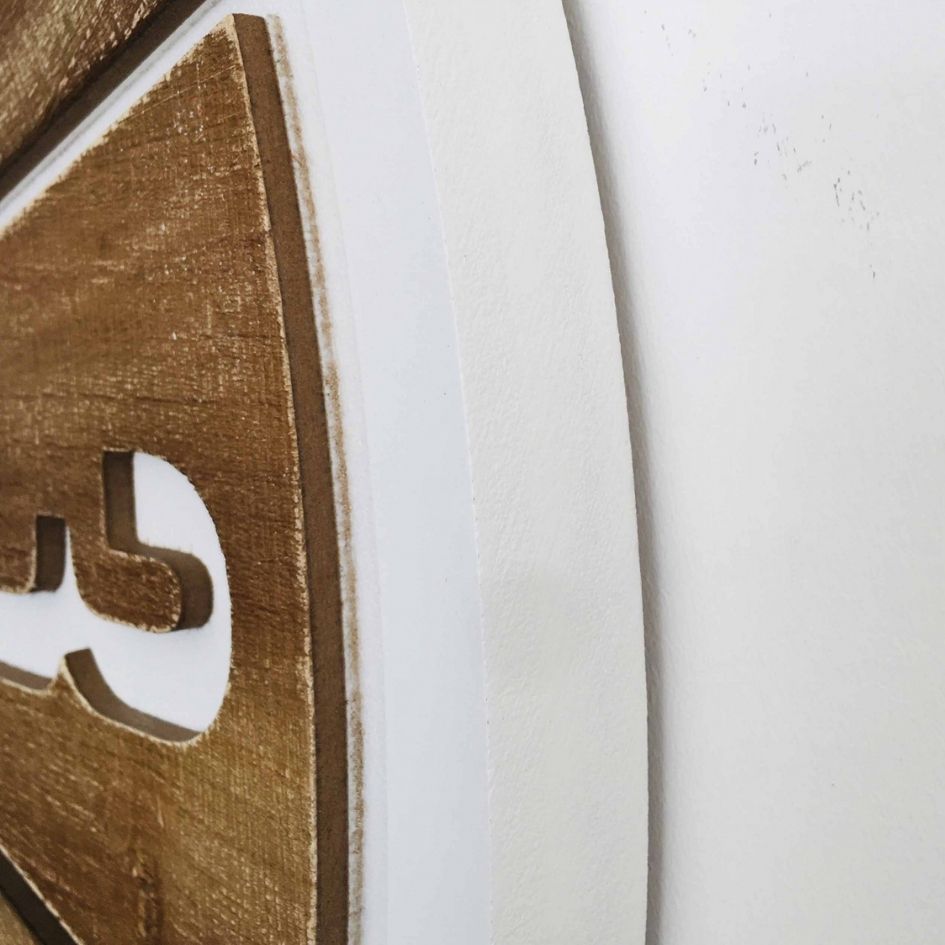 Relevo em madeira castanha com letras recortadas sobre fundo branco liso.