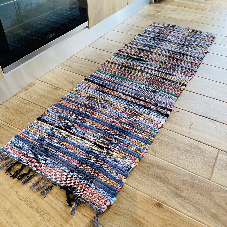 Tapete longo colorido com franjas sobre chão de madeira