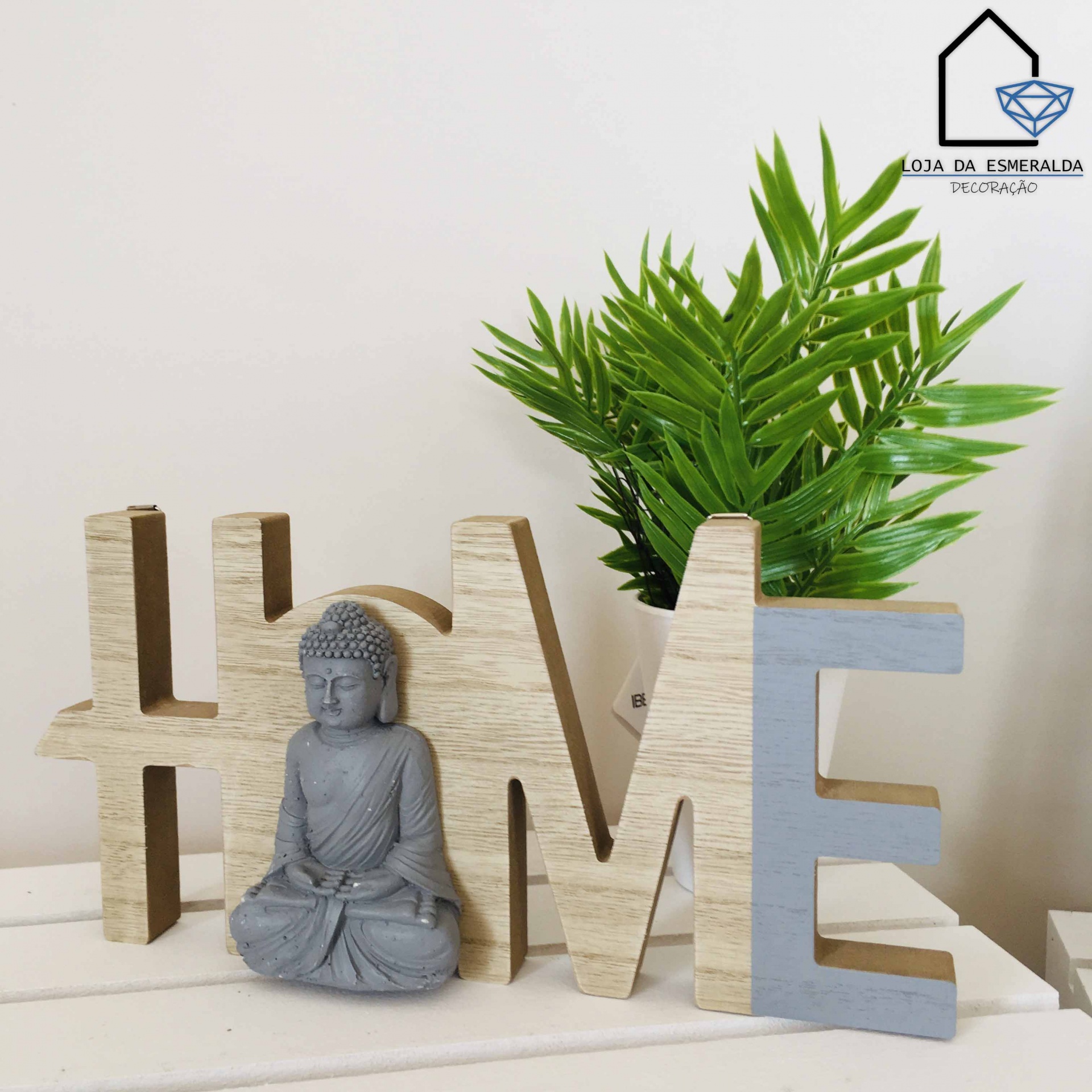 Decoração com palavra HOME em madeira e estátua de Buda cinzenta junto a plantas verdes