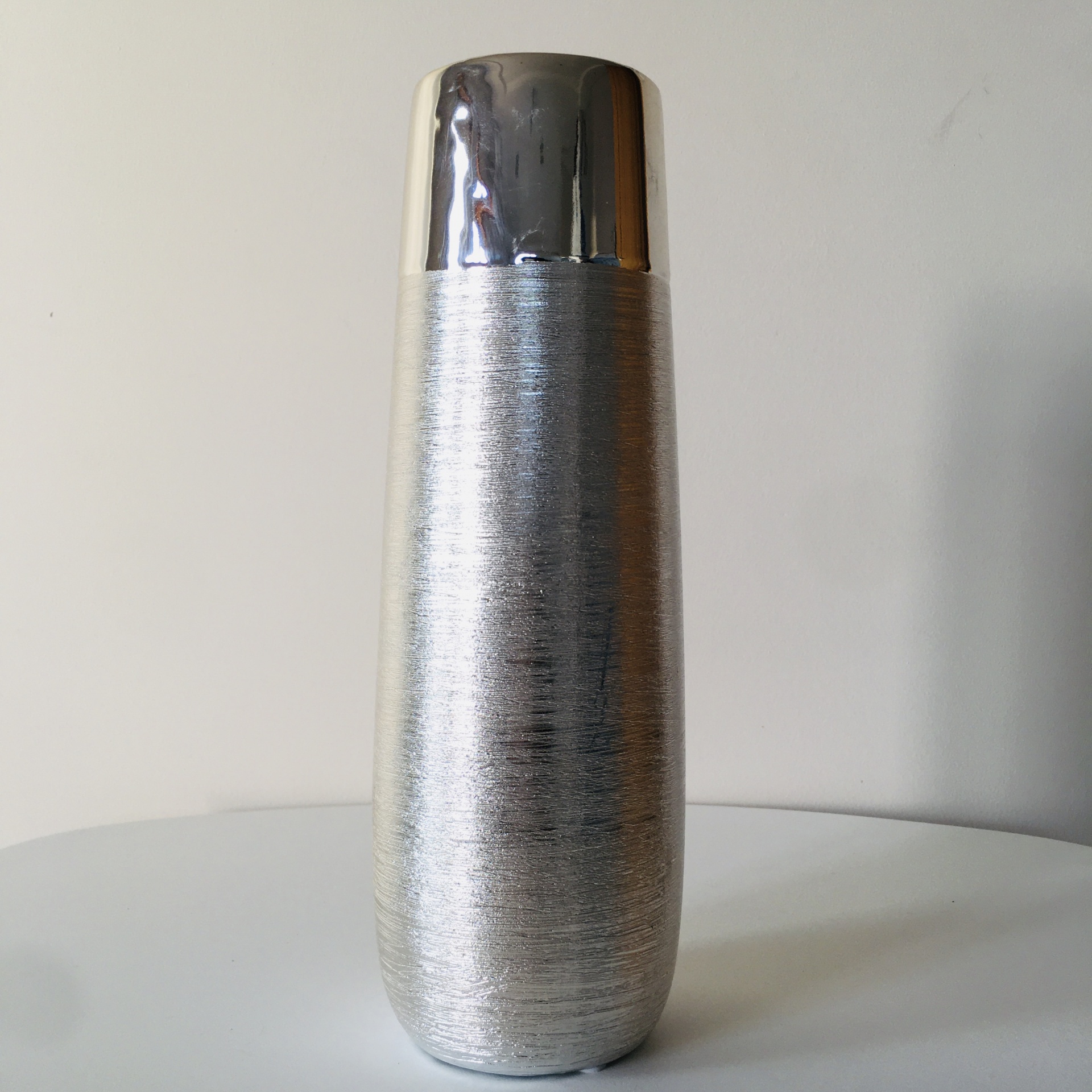 Garrafa térmica prateada com tampa metálica brilhante sobre mesa branca