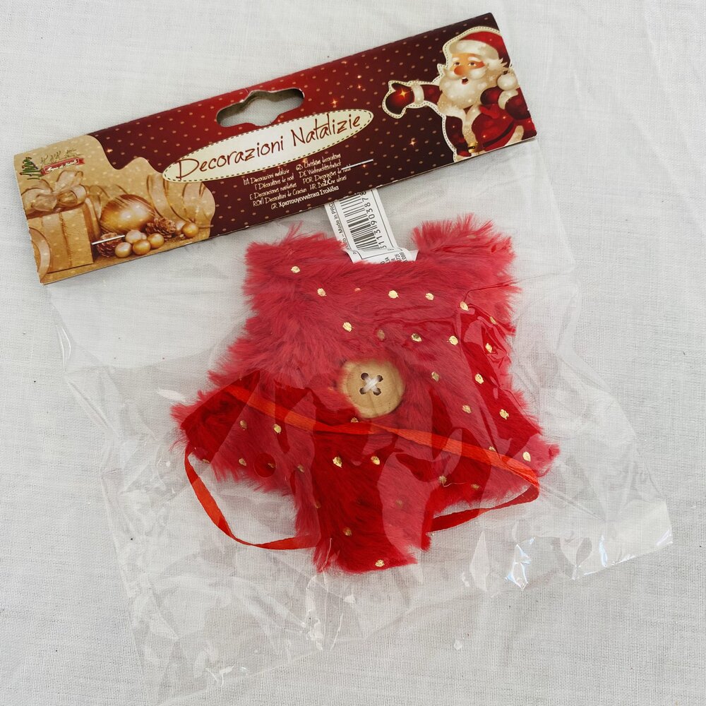 Decoração natalícia em tecido vermelho com pontos dourados e botão de urso, embalada em saco plástico transparente.