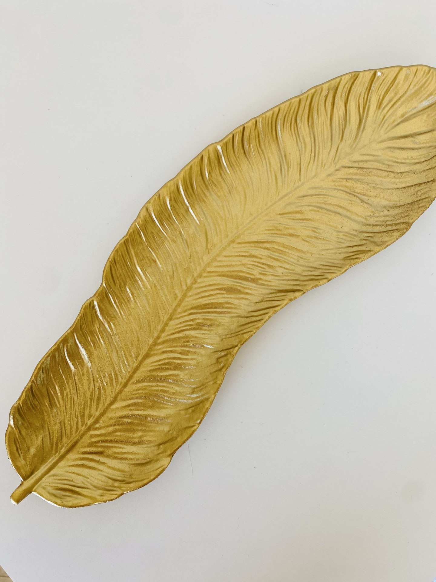 Prato decorativo dourado em forma de folha sobre superfície branca