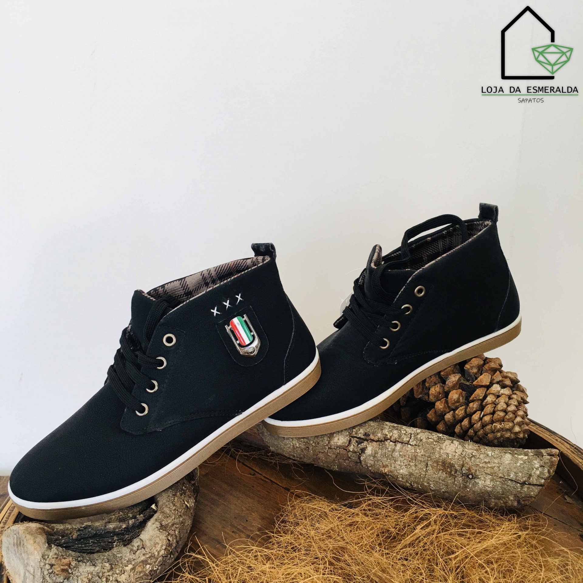 Sapatos pretos tipo ténis com sola branca e brasão colorido sobre troncos de madeira