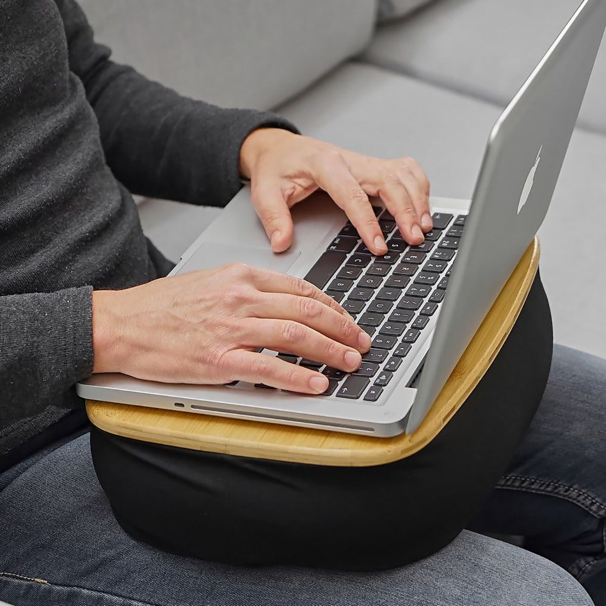 Almofada com base de madeira e almofada preta para laptop nas pernas de uma pessoa sentada