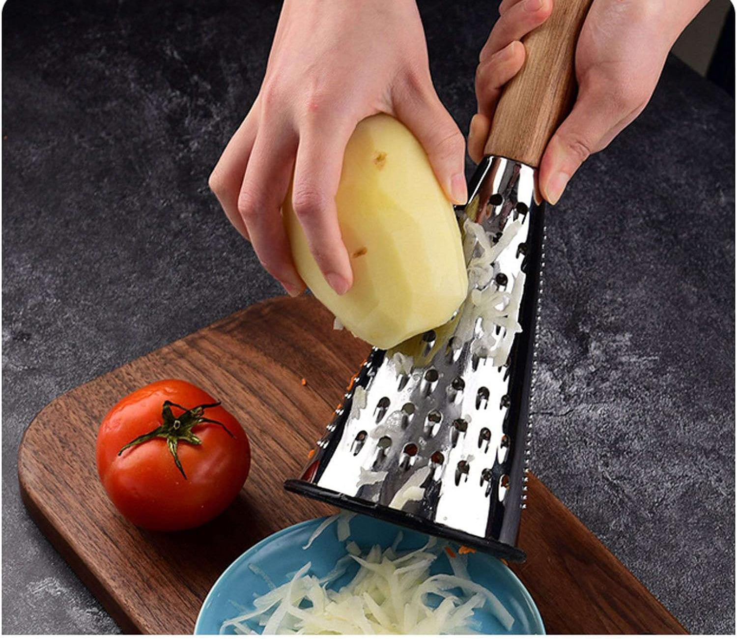 Ralador de metal com cabo de madeira a ralar batata sobre tigela azul, com tábua de madeira e tomate ao lado