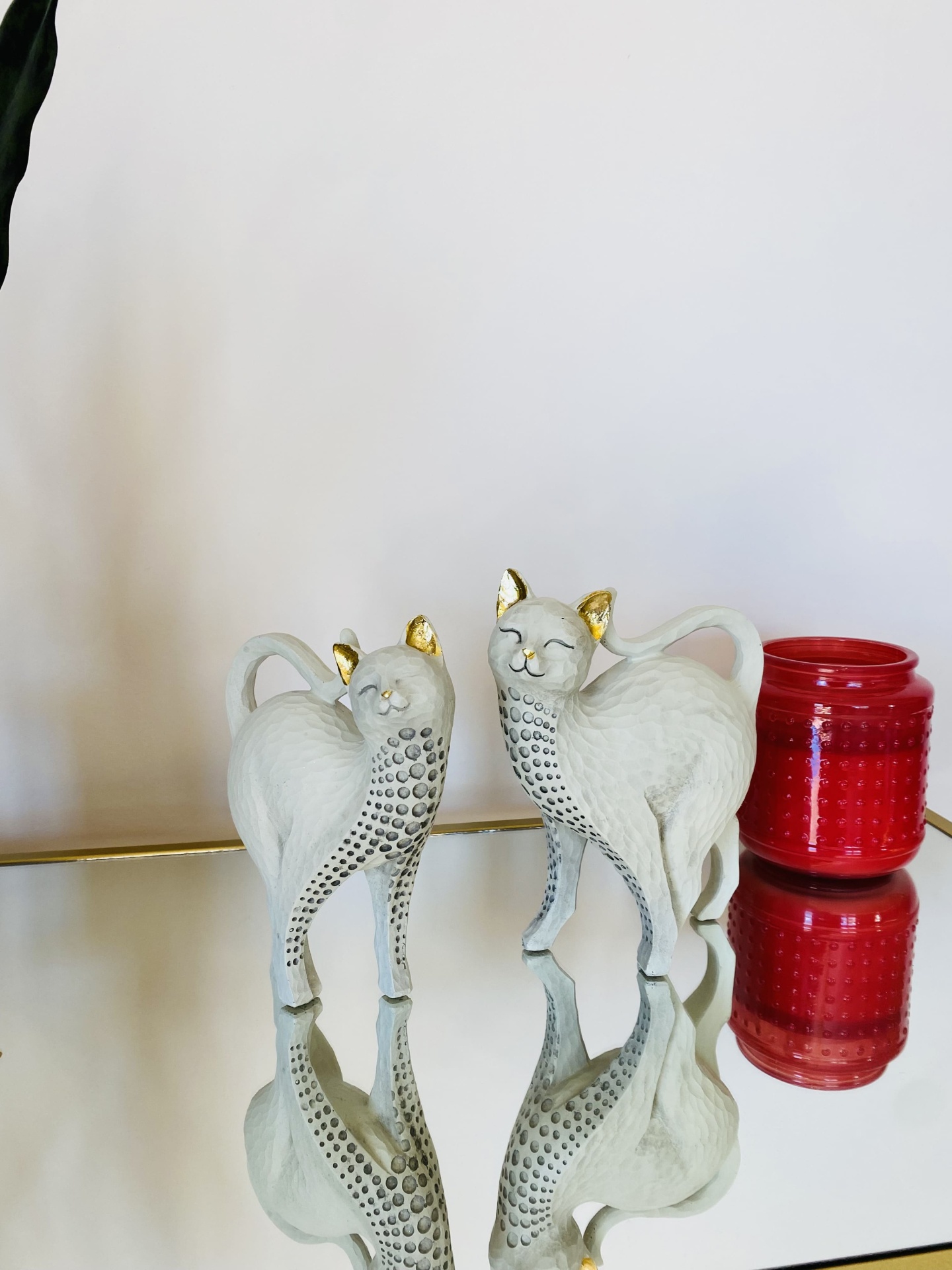Estatuetas de gatos brancas com detalhes dourados e vaso vermelho sobre espelho