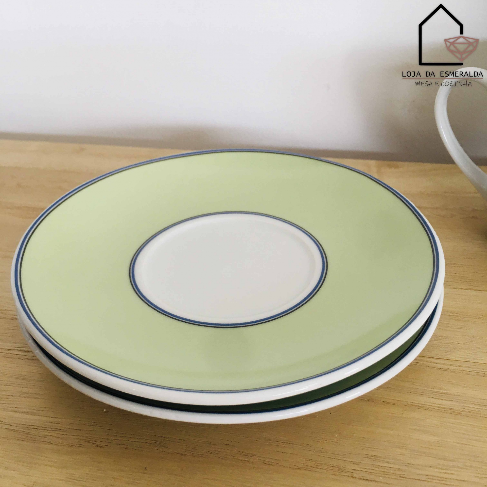 três pratos de sobremesa empilhados com bordas verdes e filetes azuis sobre superfície de madeira