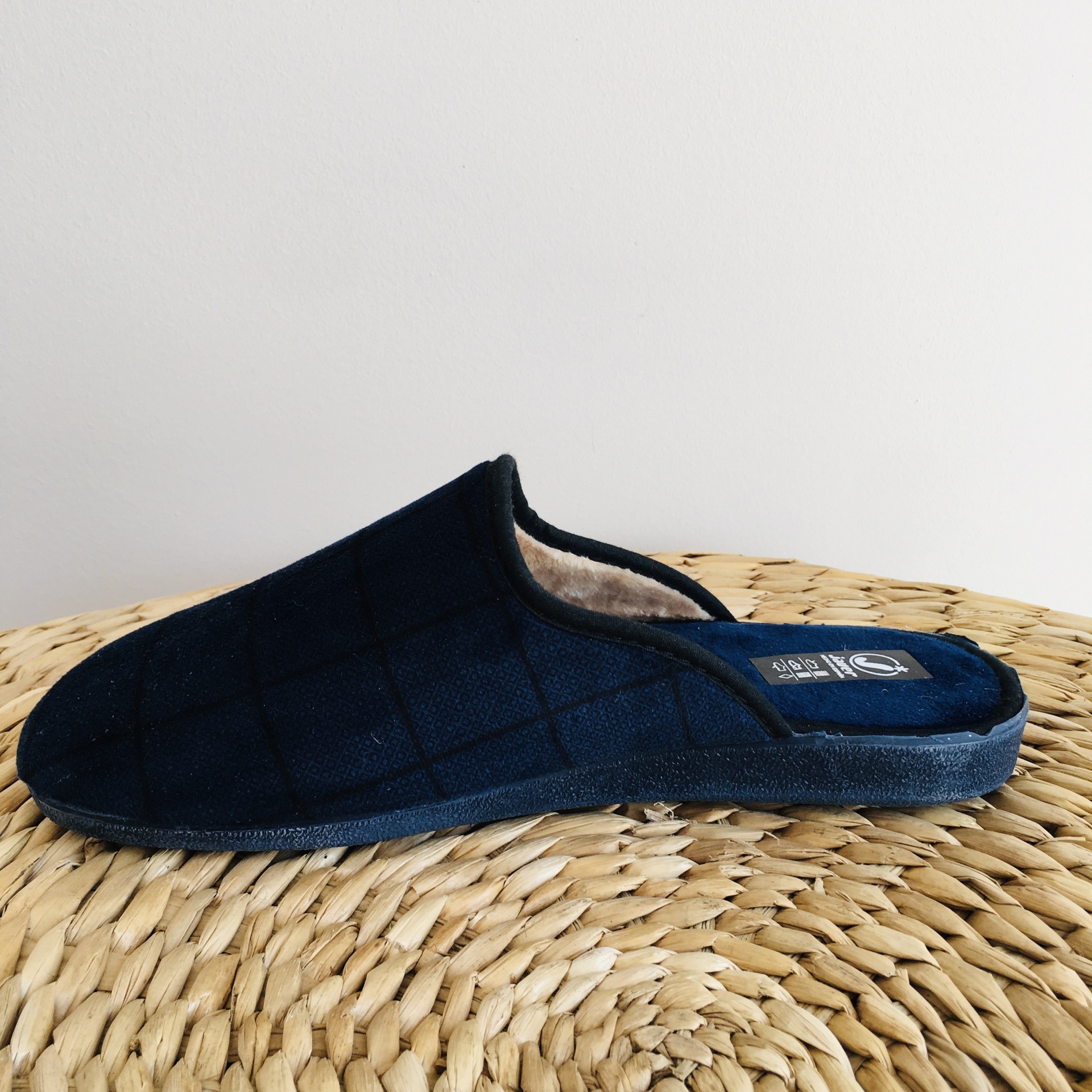 Pantufa azul escura com textura quadriculada sobre superfície trançada bege