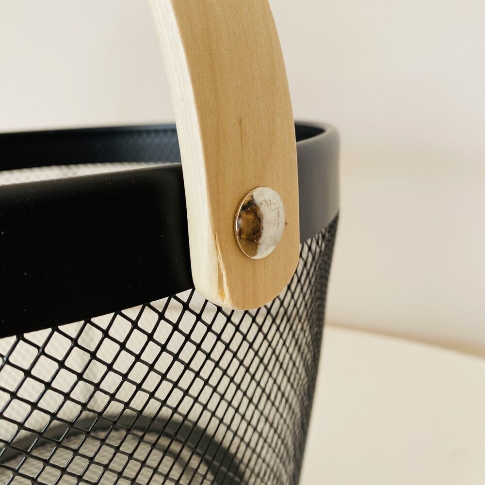Cesto preto de malha com alça de madeira numa superfície branca