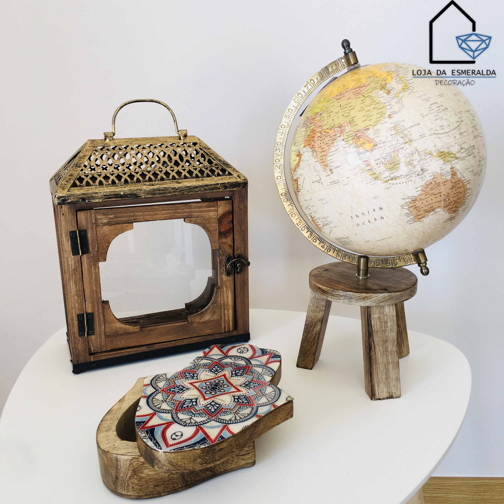 Lanterna de madeira e metal, globo terrestre em suporte de madeira e caixa decorativa com padrão colorido sobre mesa branca