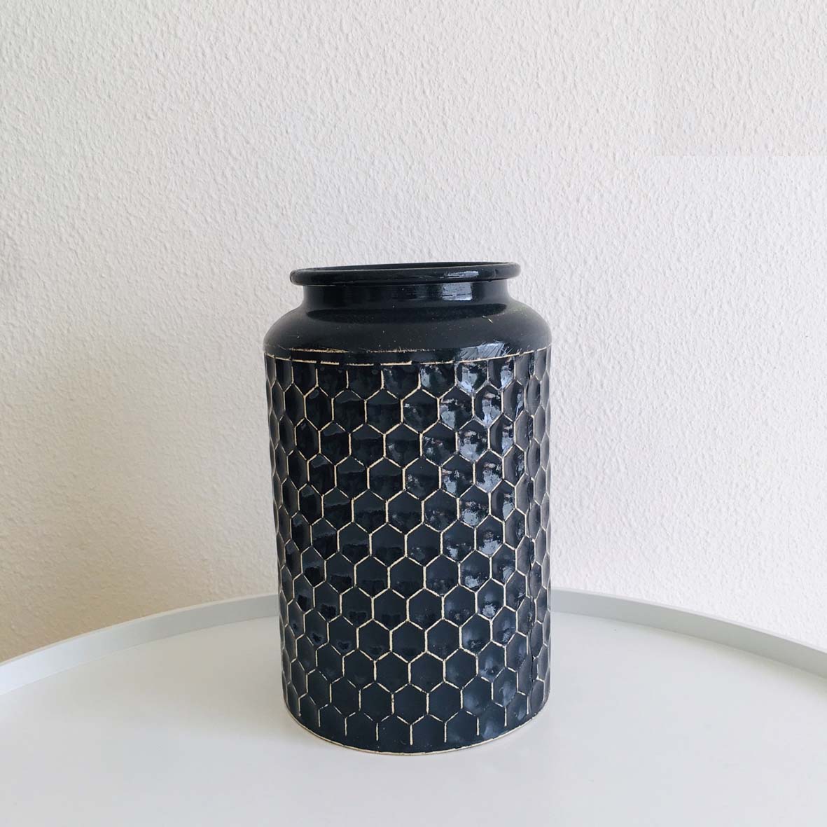 Jarro preto decorativo com padrão hexagonal dourado em relevo numa mesa branca.