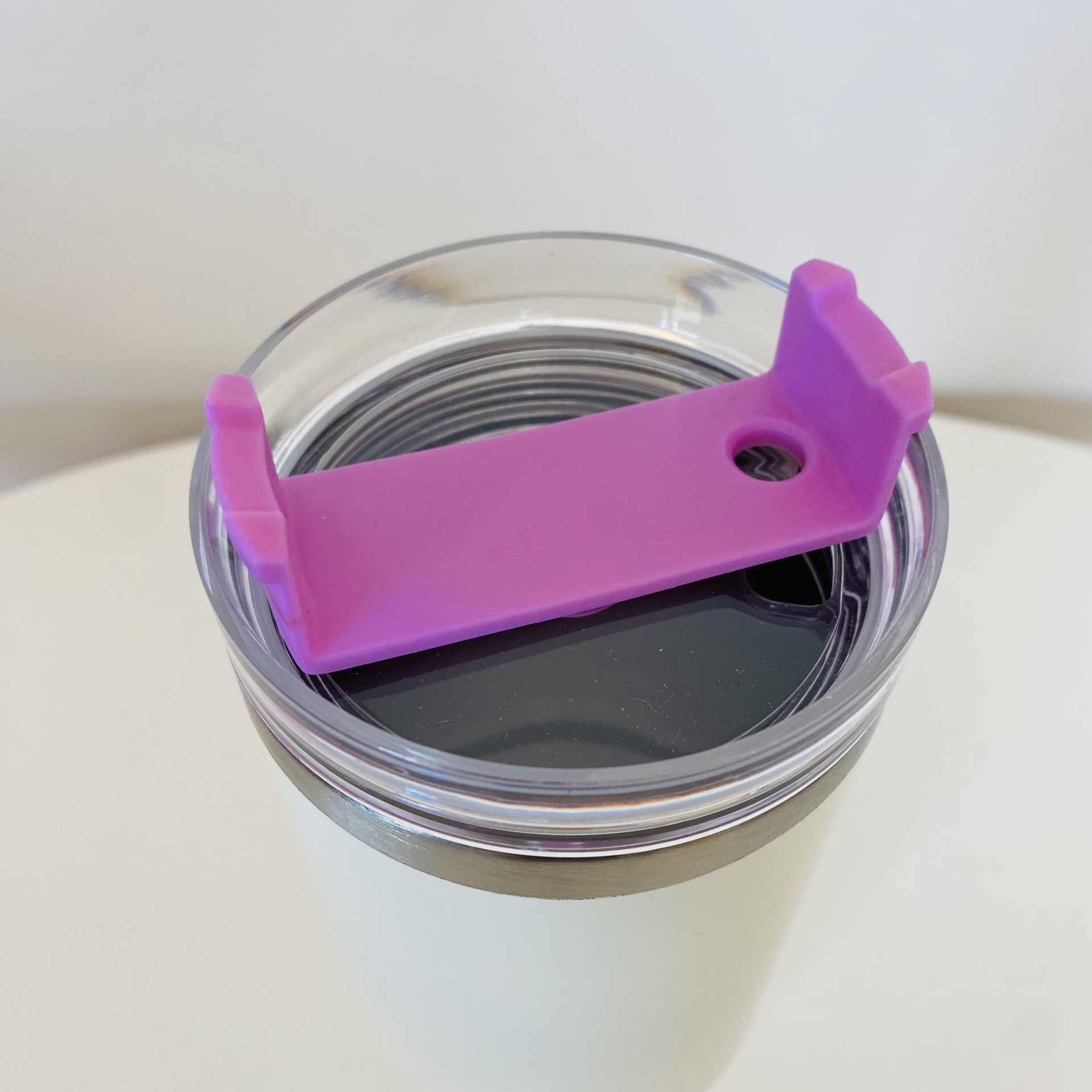 Copo térmico branco com tampa transparente e peça roxa no topo.
