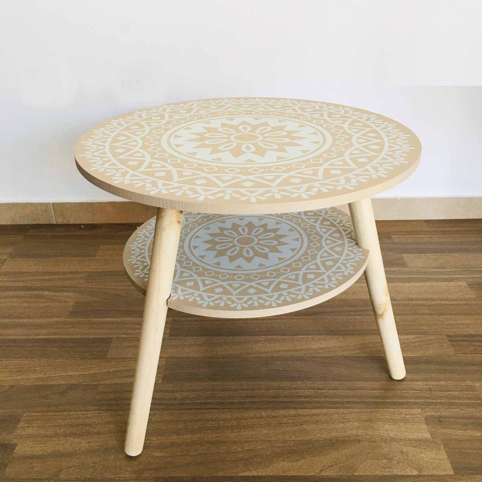 Mesa de café redonda de madeira clara com padrões brancos e três pernas sobre chão de madeira