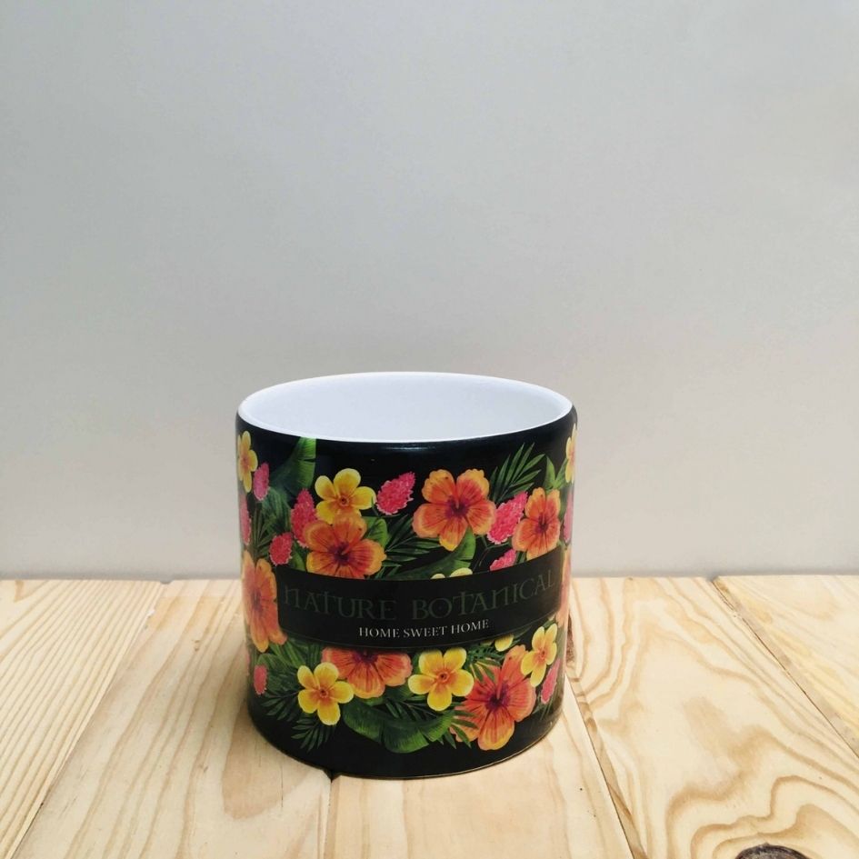Vela em recipiente de cerâmica preto com decoração floral colorida e texto, sobre superfície de madeira.