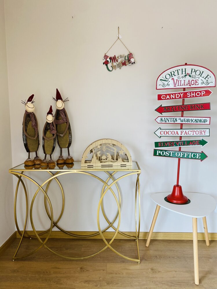 Decoração de Natal com mesa dourada, figuras de pinguins, cena de madeira natalícia e placa colorida indicativa do Polo Norte.