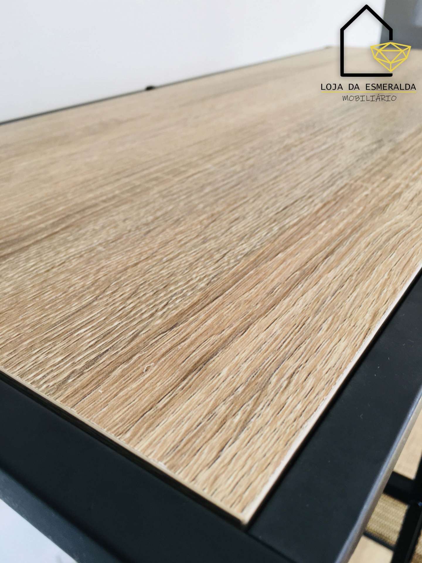 Mesa de madeira clara com estrutura metálica preta e logotipo da loja no canto superior direito