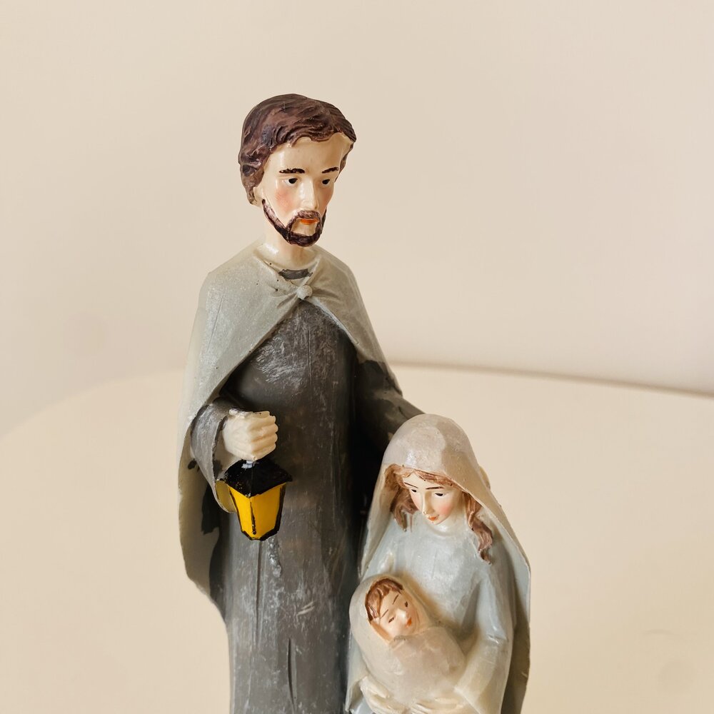 Figura decorativa religiosa da Sagrada Família em cores neutras com lâmpada amarela.