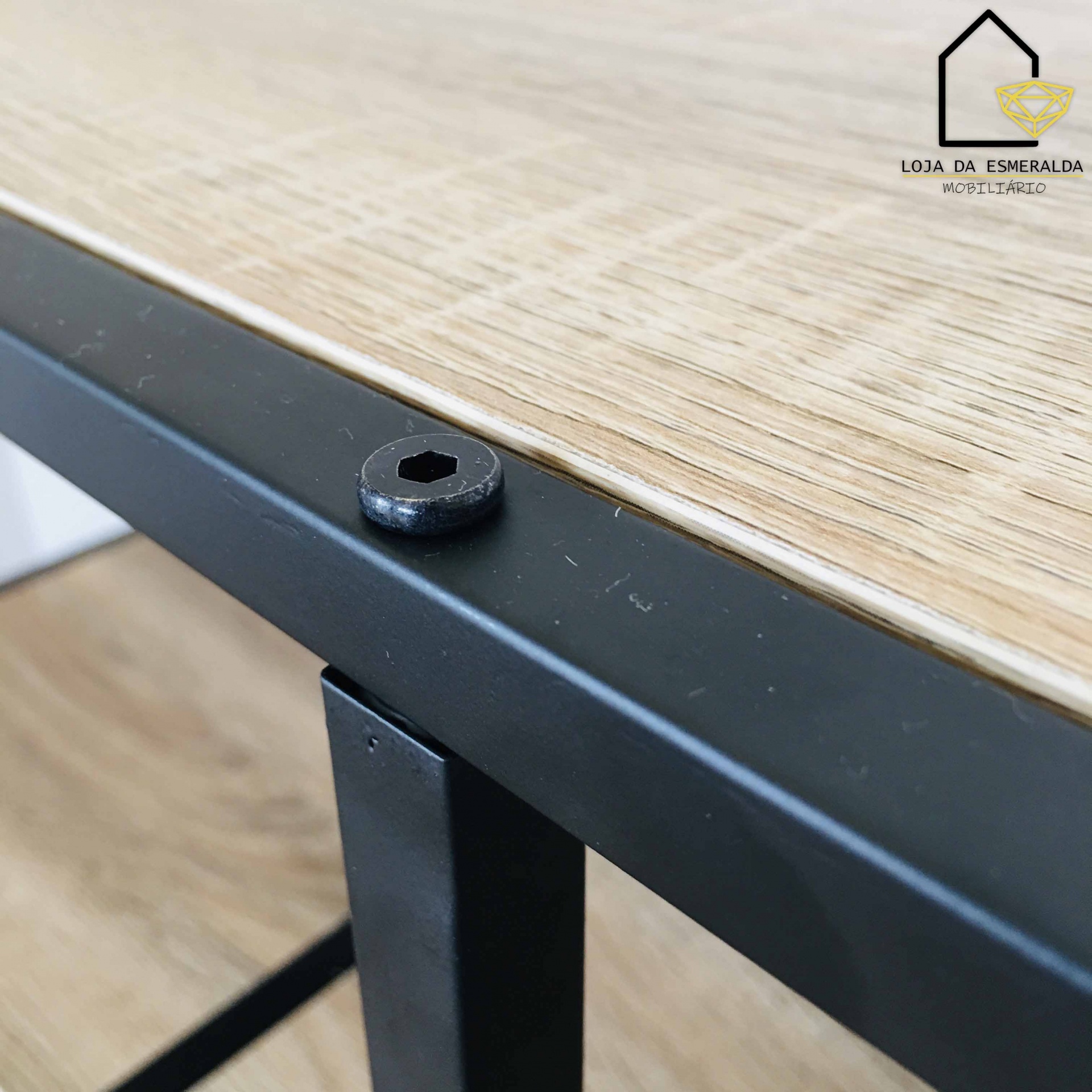 Mesa de madeira clara com base metálica preta e parafuso visível