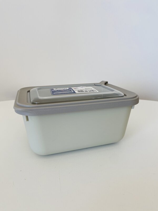 Recipiente de plástico com tampa cinzenta e corpo branco sobre uma superfície branca