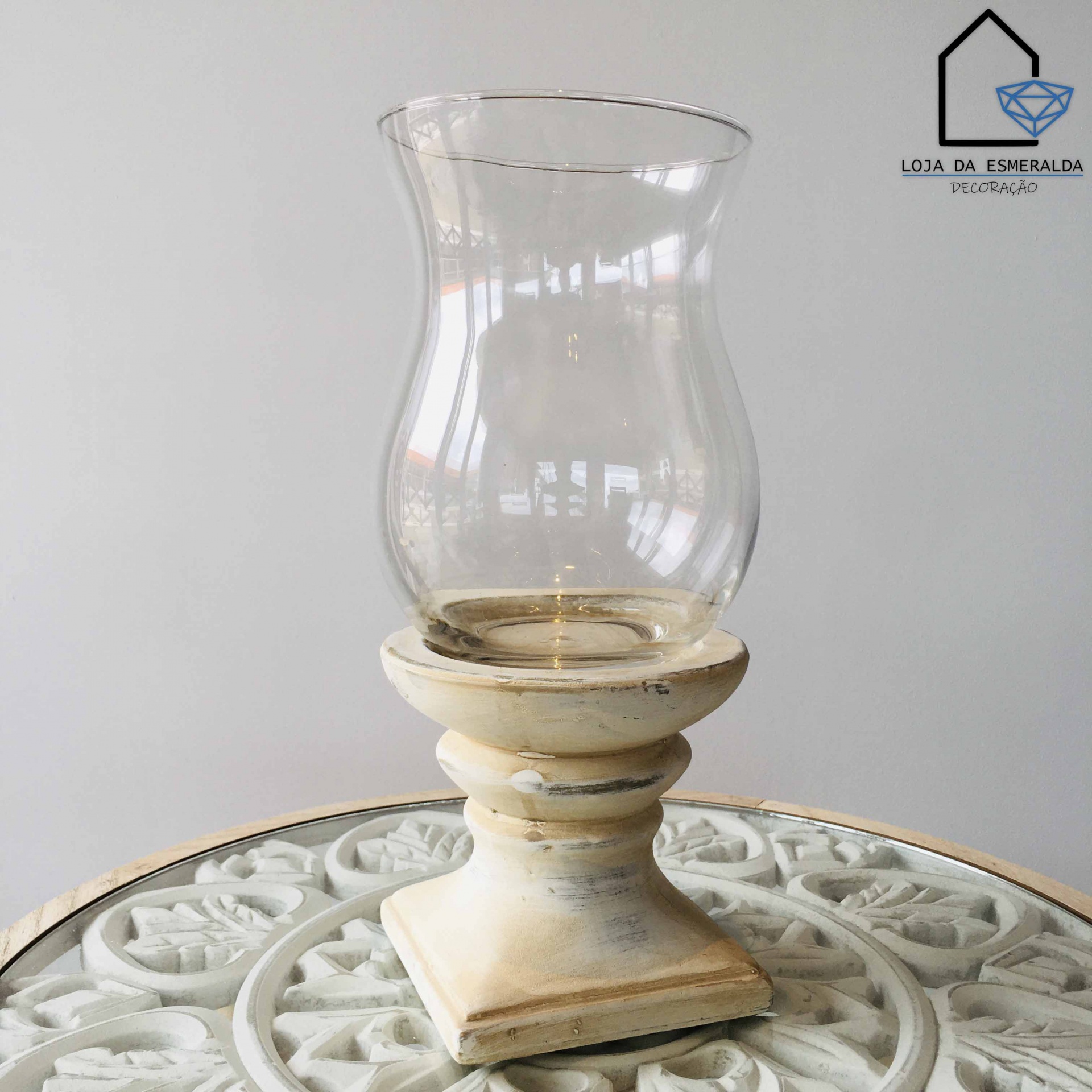 Castiçal de madeira branca envelhecida com copo de vidro transparente sobre superfície branca decorativa