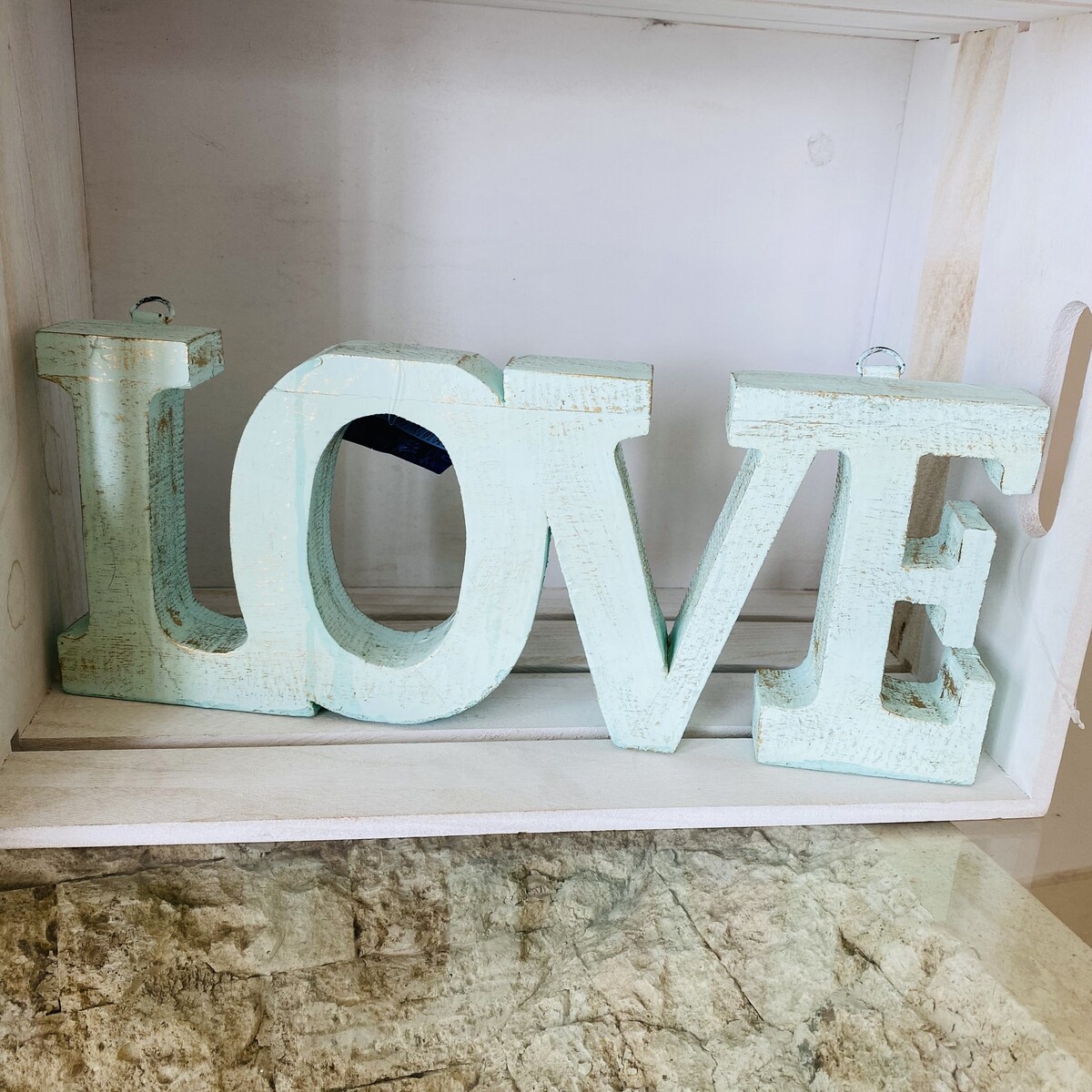 Objeto decorativo de madeira branco com a palavra LOVE, numa prateleira branca