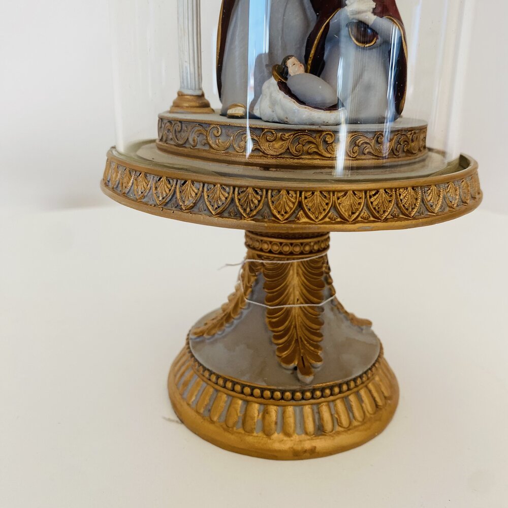 Peça decorativa em vidro com base dourada e cena de presépio dentro de globo de vidro