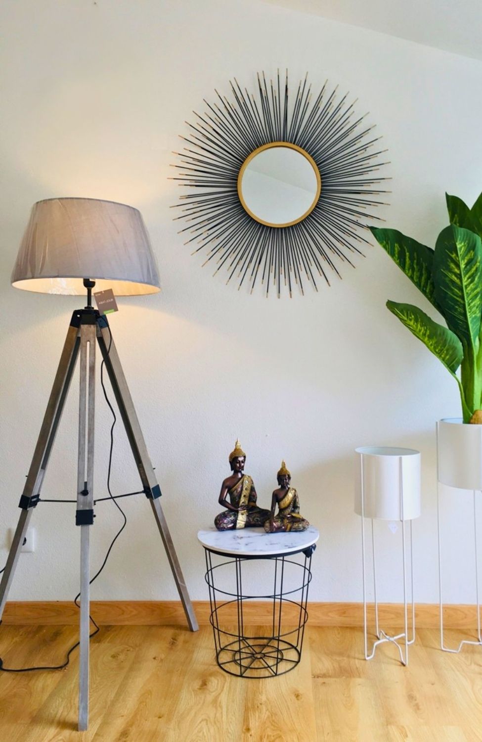 Lâmpada de pé com base tripé, espelho decorativo circular e mesa pequena com estátuas e plantas