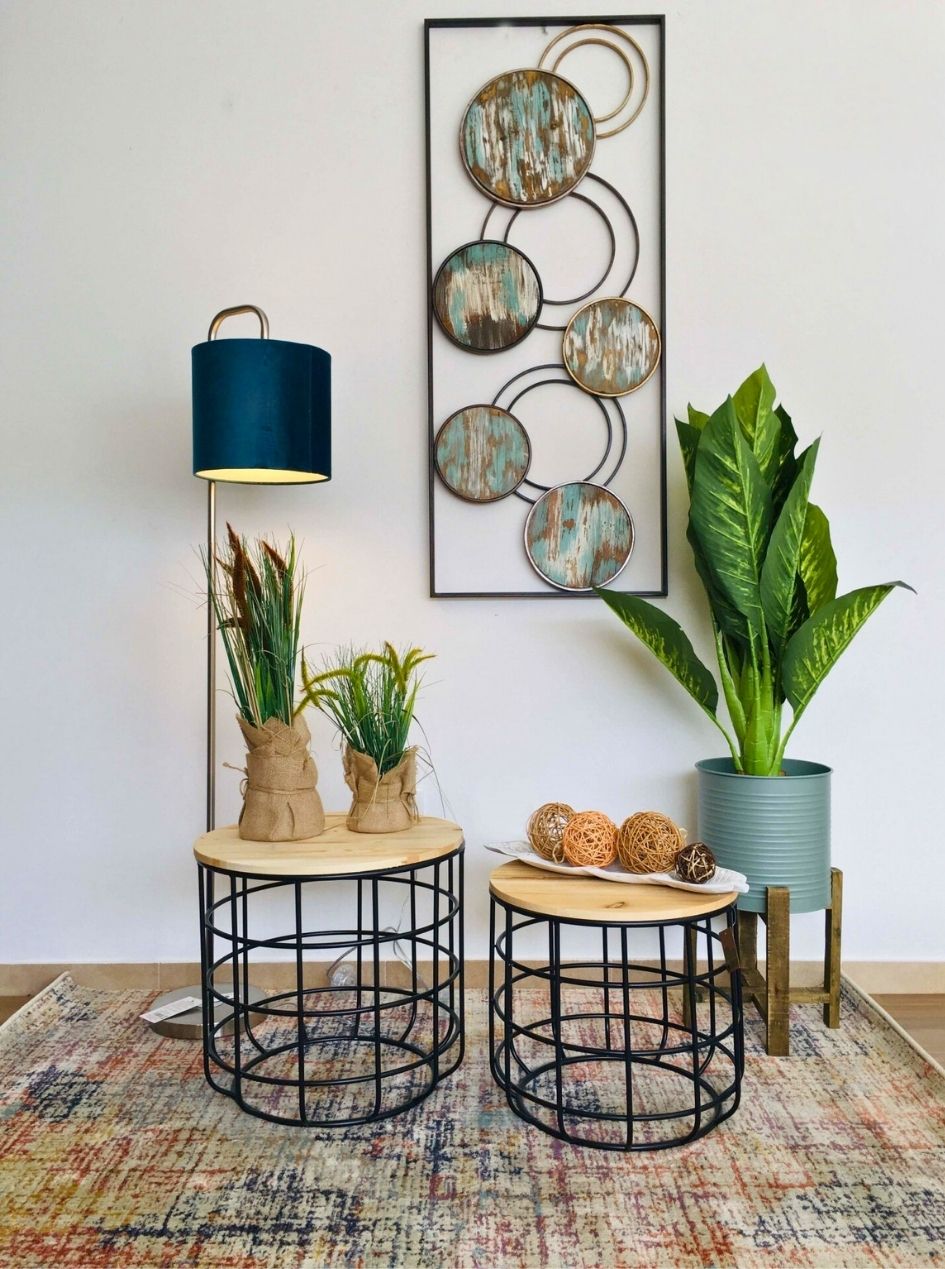 Mesa de centro dupla com tampo de madeira, vasos de plantas, lâmpada de pé azul e quadro decorativo circular na parede