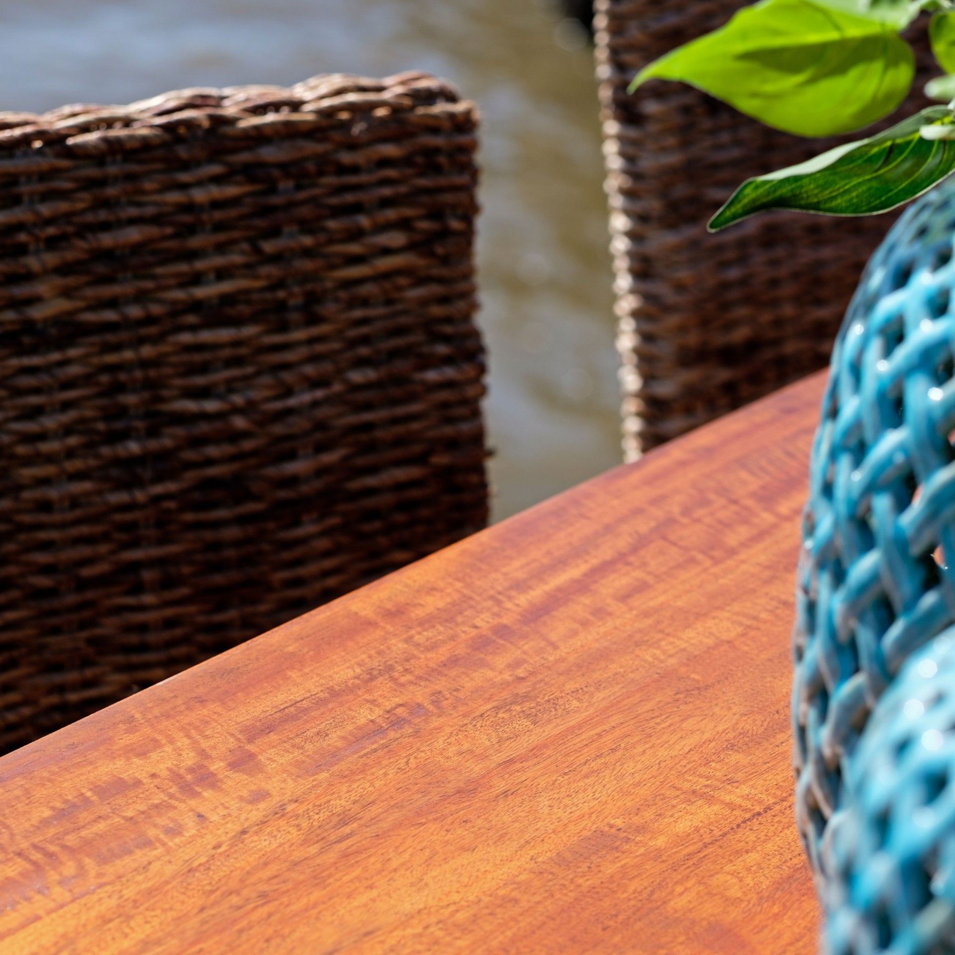 Mesa de madeira com cadeiras de vime e vaso azul trançado com folhas verdes