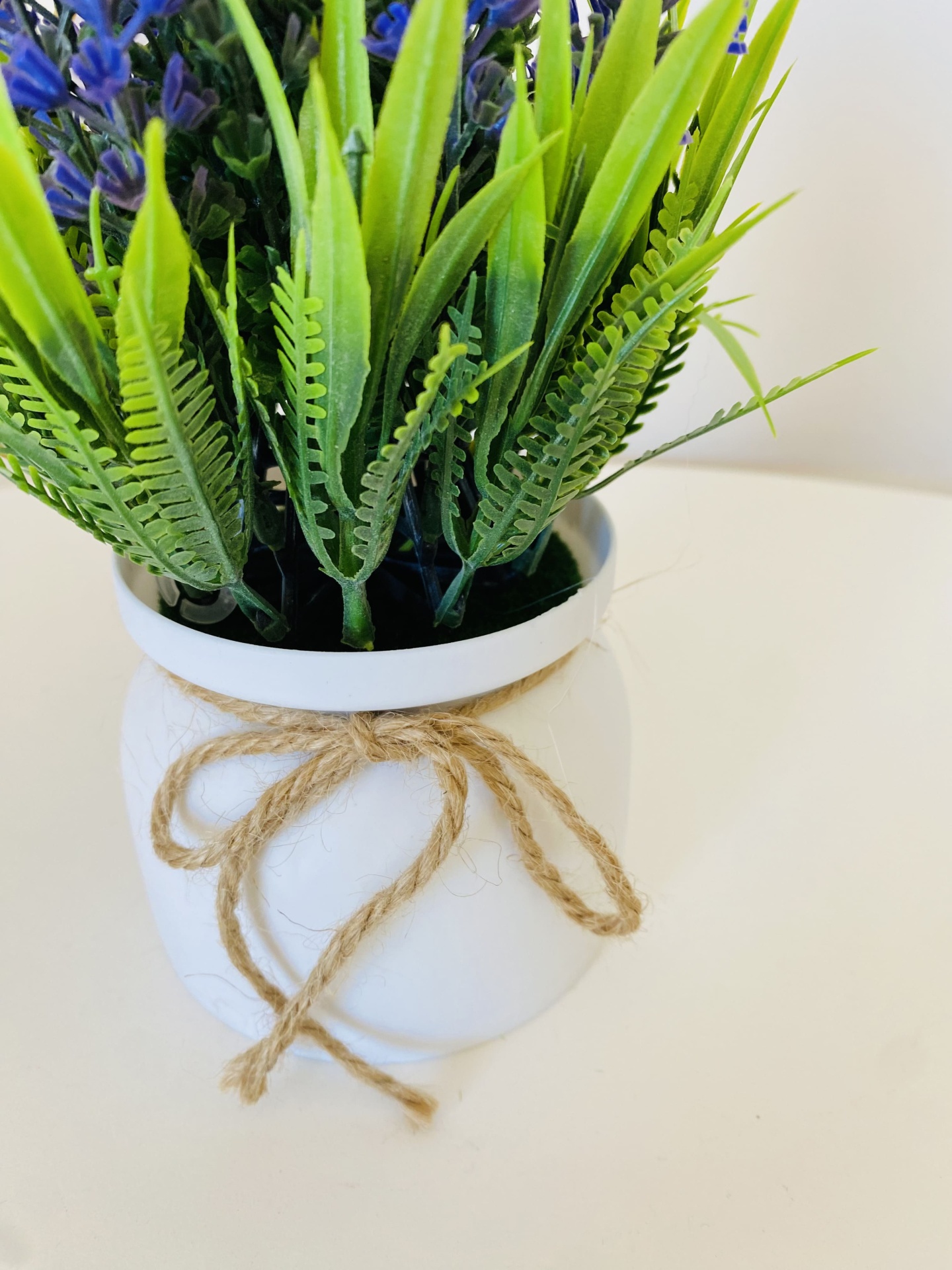 Vaso branco com laço de corda e plantas artificiais verdes com flores roxas
