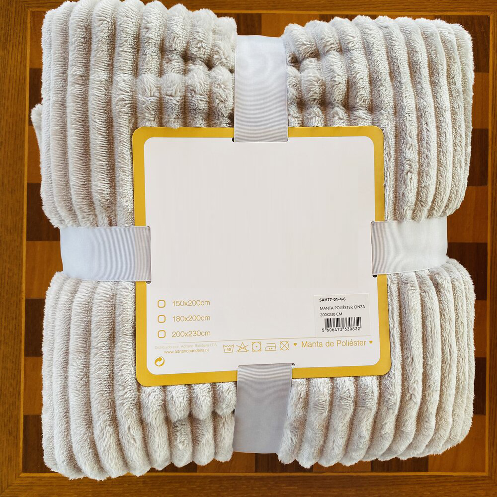 Cobertor creme claro com riscas em relevo e etiqueta amarela sobre madeira clara