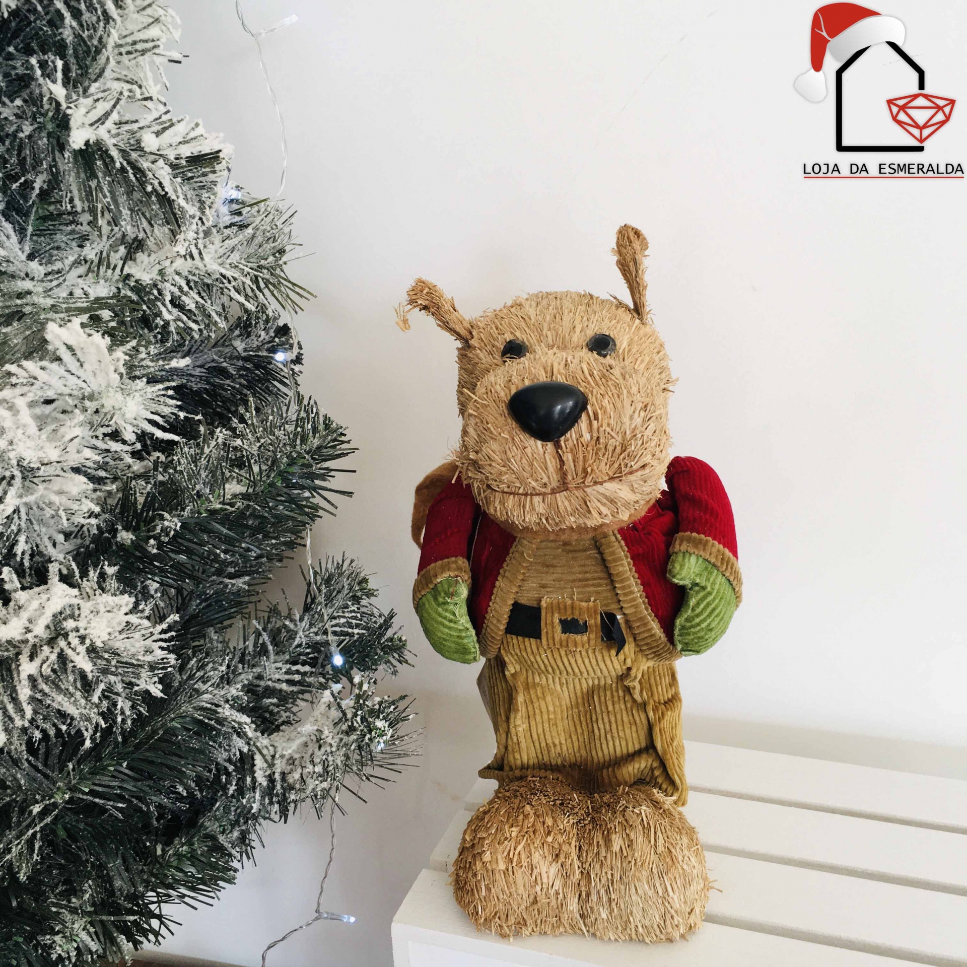 Estatueta decorativa de cão em material natural junto a árvore de Natal nevada.