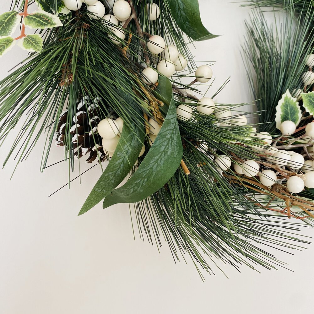 Ramo decorativo com folhas verdes, bagas brancas e pinhas