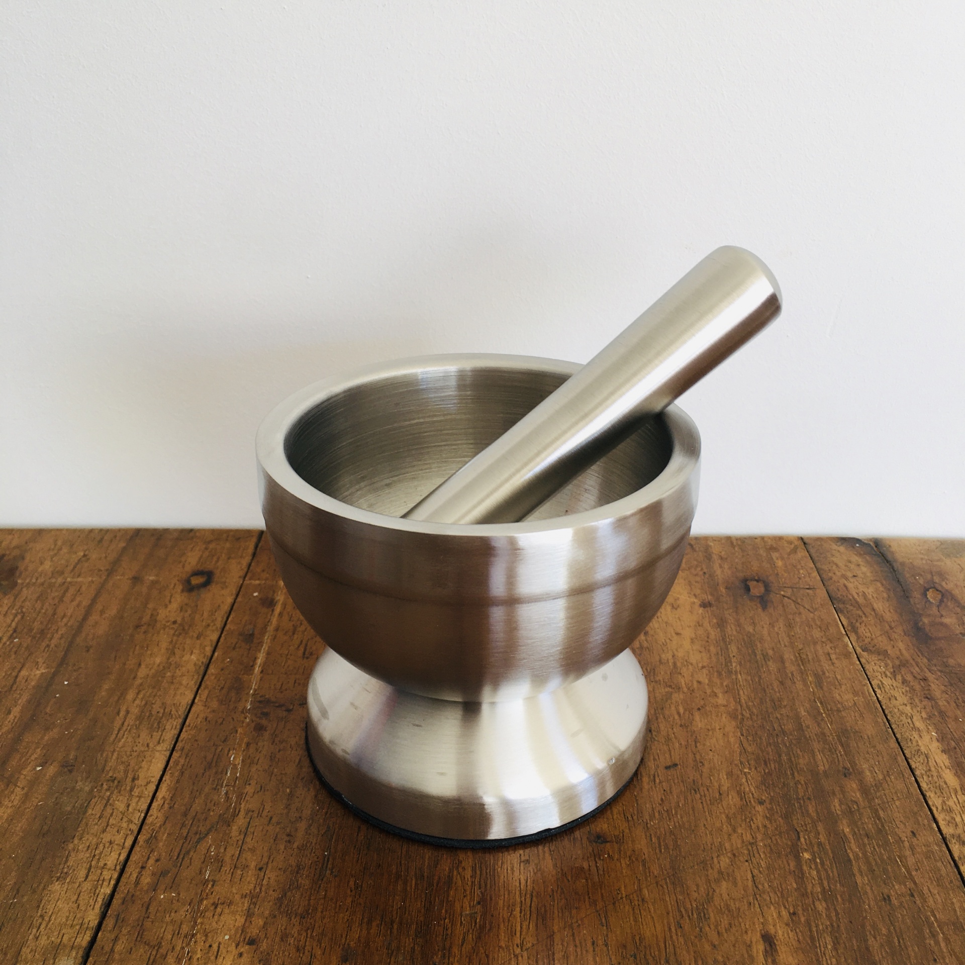 Pilão e almofariz de metal prateado sobre mesa de madeira